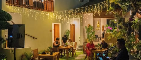 An outdoor seating area with tables and chairs, string lights, and potted plants.