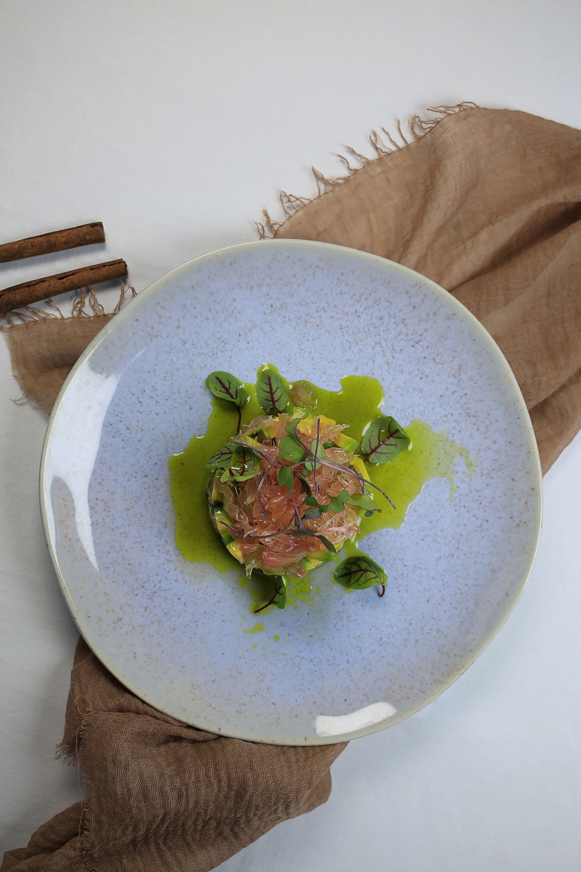 Un plato de comida con salsa verde, adornado con hojas y posiblemente carne, sobre un plato de cerámica con manchas.