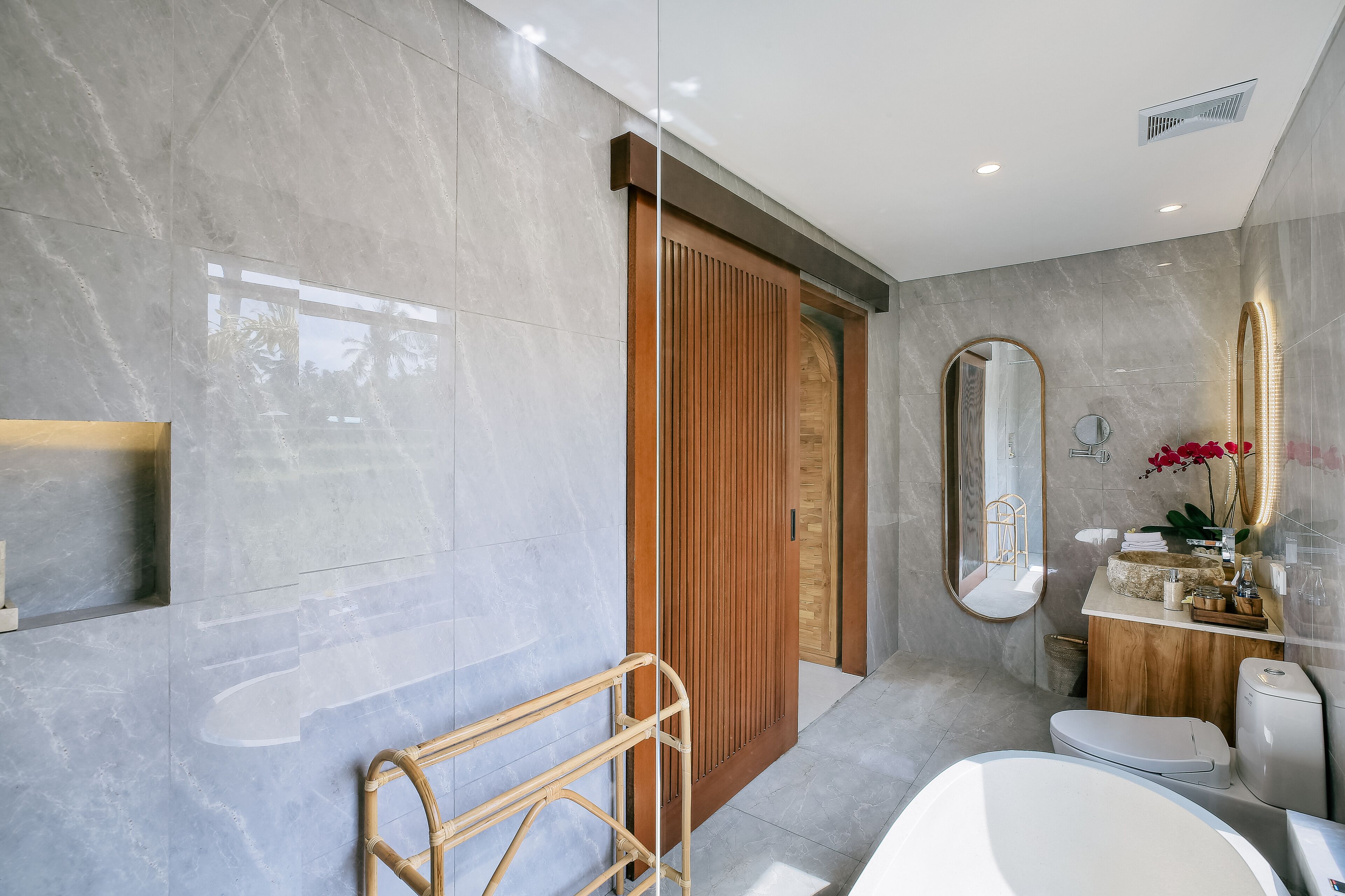 A modern bathroom with a large mirror, a wooden door, and a toilet.