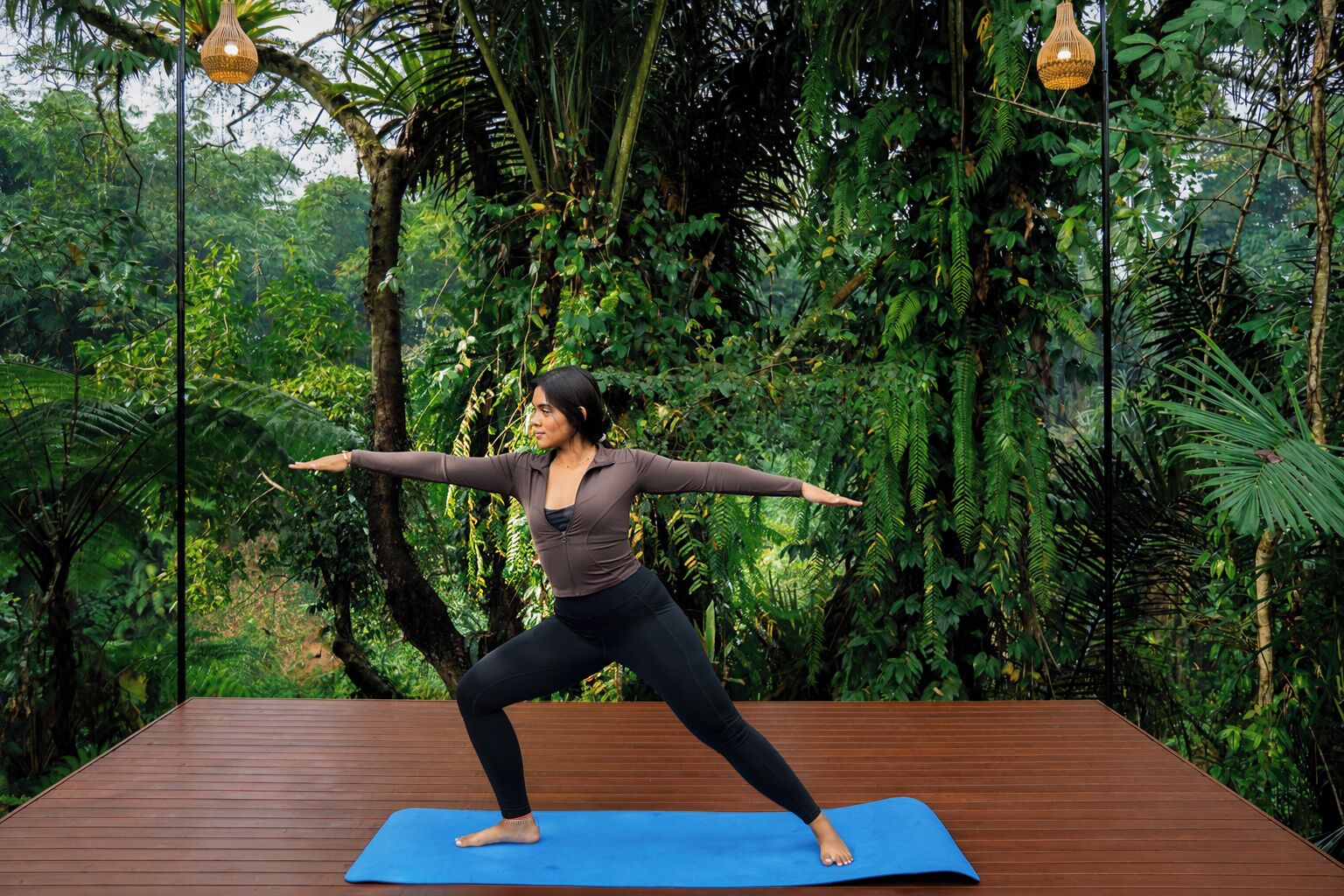 Una persona realizando una postura de yoga sobre una colchoneta azul al aire libre, con abundante vegetación de fondo.