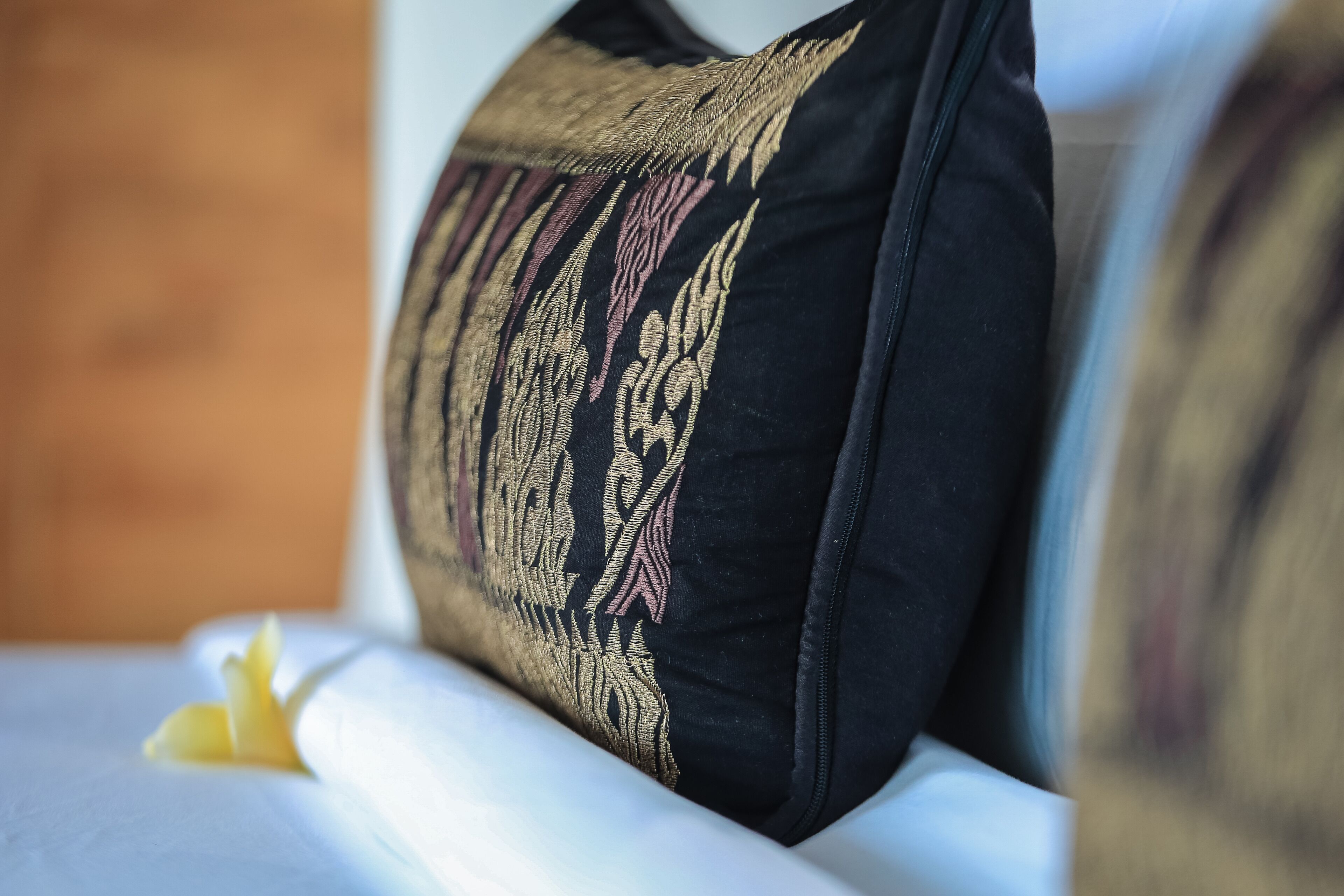 A close-up of a black pillow with gold embroidery on a bed.