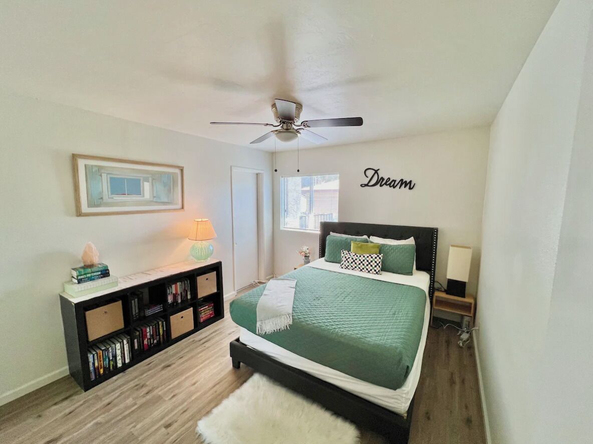 Une chambre à coucher avec un lit, une bibliothèque, un ventilateur de plafond et un mur sur lequel est écrit le mot « Rêve ».