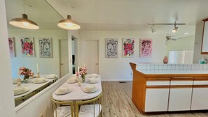 A dining area with a round table set for four, a kitchen island, and artwork on the walls.