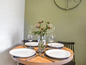 Une table de salle à manger ronde, avec de l’assiette blanche, des couverts et trois vases en verre transparent contenant des fleurs et des plantes vertes.