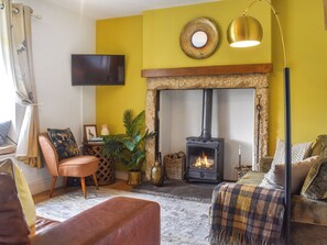 Una sala de estar con chimenea, televisor montado en la pared y un rincón de descanso acogedor con sofá y sillón.