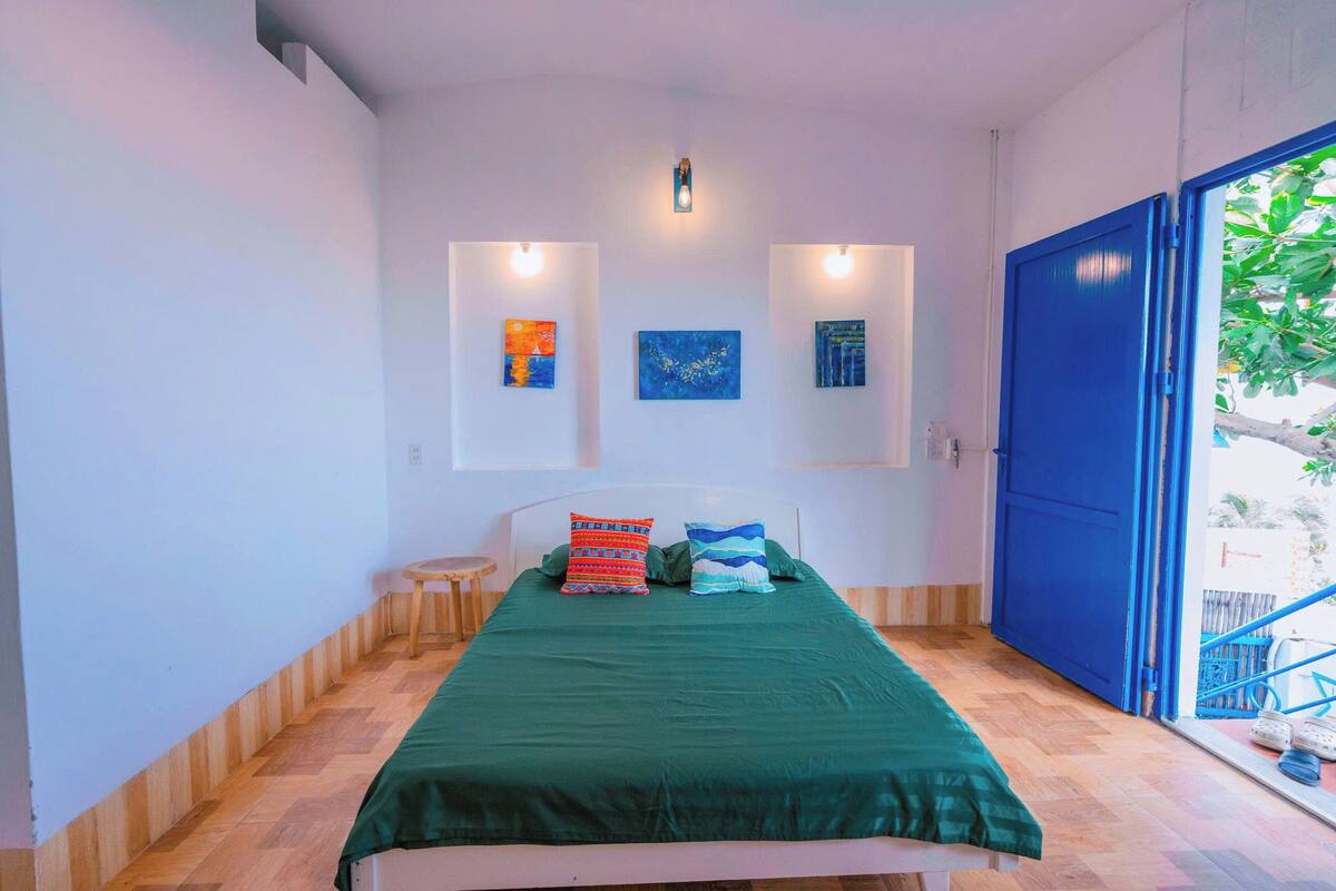 Une pièce avec un lit, un petit tabouret et une porte bleue.