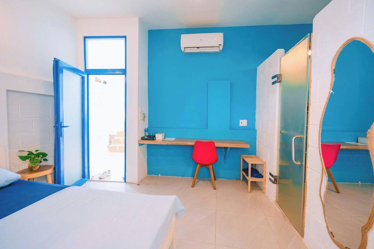 Une pièce comprenant un lit, un bureau, une chaise, une petite table avec une plante et un miroir.