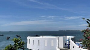 A white building with a pool, overlooking a calm sea with boats. - Irini Homestay & Hotel Mui Ne (Mui Ne)
