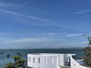 A white building with a pool, overlooking a calm sea with boats. - Irini Homestay & Hotel Mui Ne (Mui Ne)