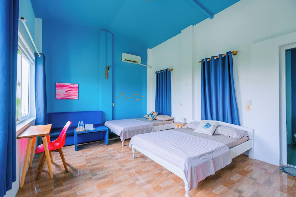 Une chambre avec deux lits, une petite table, une chaise et une fenêtre avec des rideaux.