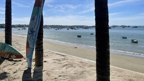 A beach with palm trees, a surfboard, and boats in the water. - Irini Homestay & Hotel Mui Ne (Mui Ne)