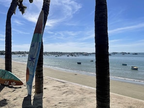 A beach with palm trees, a surfboard, and boats in the water. - Irini Homestay & Hotel Mui Ne (Mui Ne)