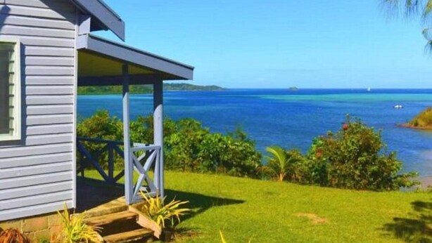 Ein Küstenhaus mit Veranda mit Blick auf ein klares blaues Meer und eine entfernte Insel.