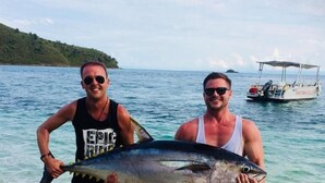 Zwei Personen halten einen großen Fisch in flachem Wasser, im Hintergrund ein Boot.