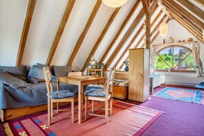 A cozy attic bedroom with a sloped ceiling, a wooden table, two chairs, a sofa, a window with curtains, and a view of greenery outside. - Holiday Studio 'Im Haus Ginkgo' with Shared Pool, Shared Garden and Wi-Fi (Wittstock/Dosse)