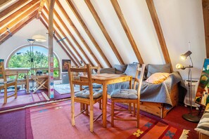 A cozy attic bedroom with a wooden table, chairs, a bed, and a large window. - Holiday Studio 'Im Haus Ginkgo' with Shared Pool, Shared Garden and Wi-Fi (Wittstock/Dosse)