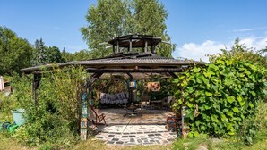 Et hyggeligt udendørs opholdsområde med fliseterrasse, træmøbler og et overdækket område.