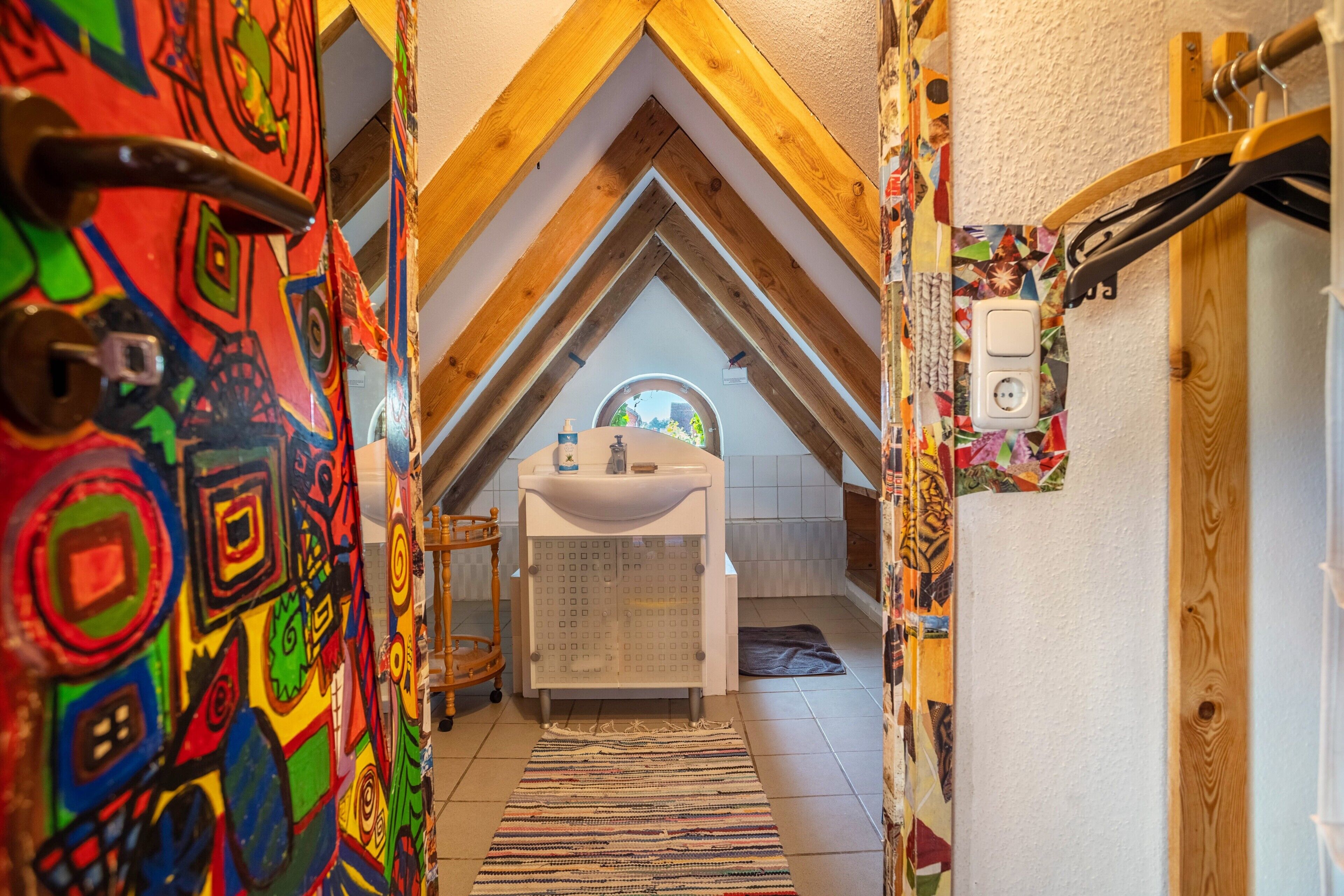 A narrow hallway with a sloped ceiling, a small sink, and a window.