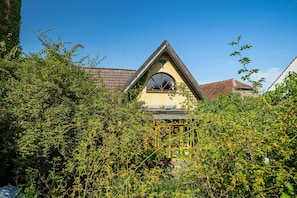 A building with a triangular roof, a large arched window, and surrounded by dense foliage. - Holiday Studio 'Im Haus Ginkgo' with Shared Pool, Shared Garden and Wi-Fi (Wittstock/Dosse)