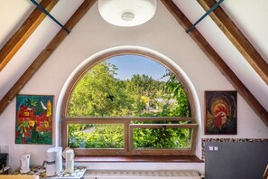 Ein Zimmer mit einem großen Bogenfenster, Holzbalken, einem Deckenventilator und zwei Bildern an den Wänden.