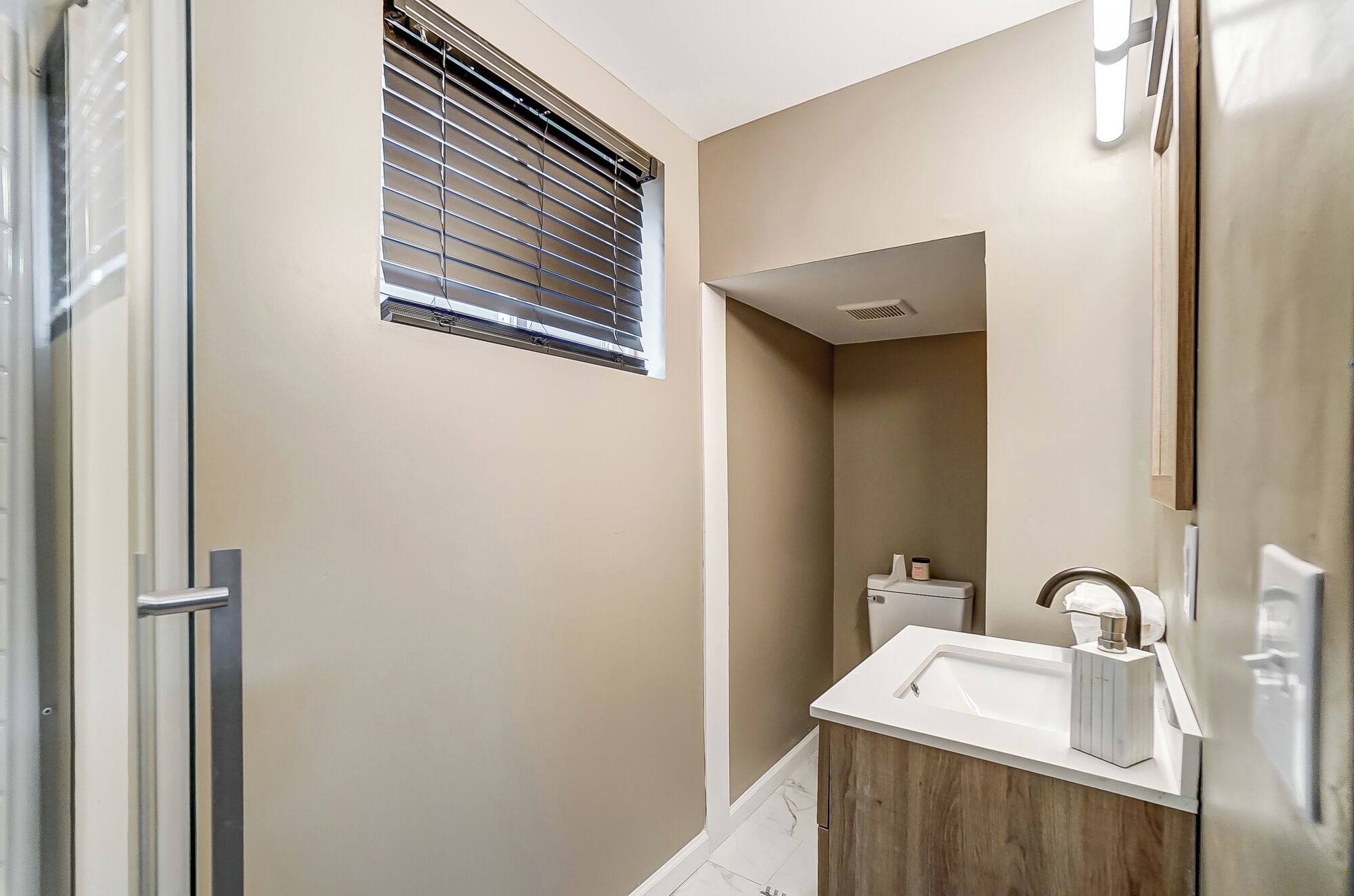 Une petite salle de bain avec des toilettes, un lavabo et une fenêtre équipée de stores.