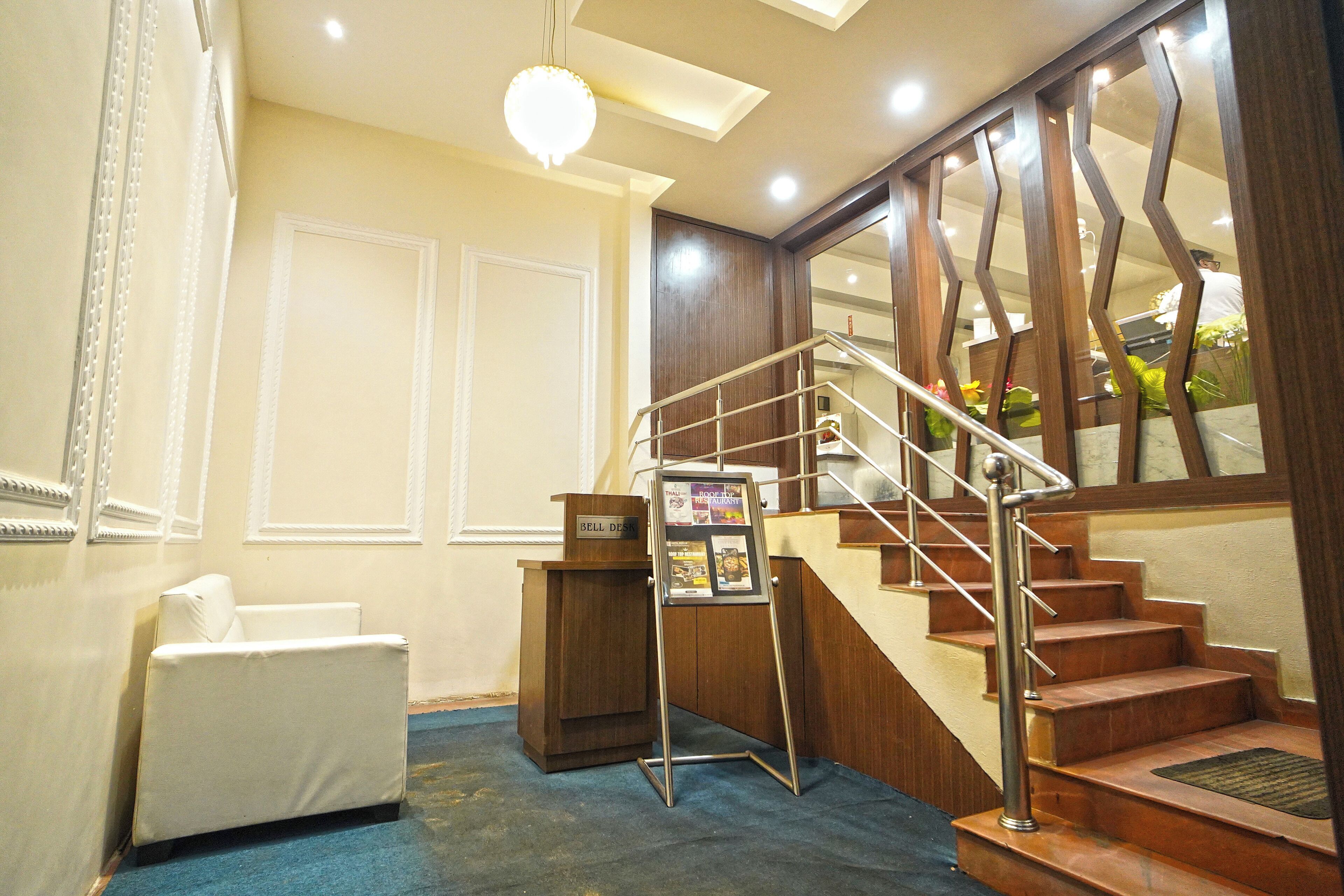 Un vestíbulo de hotel con una escalera, una recepción, un sofá blanco y un tablón de anuncios.