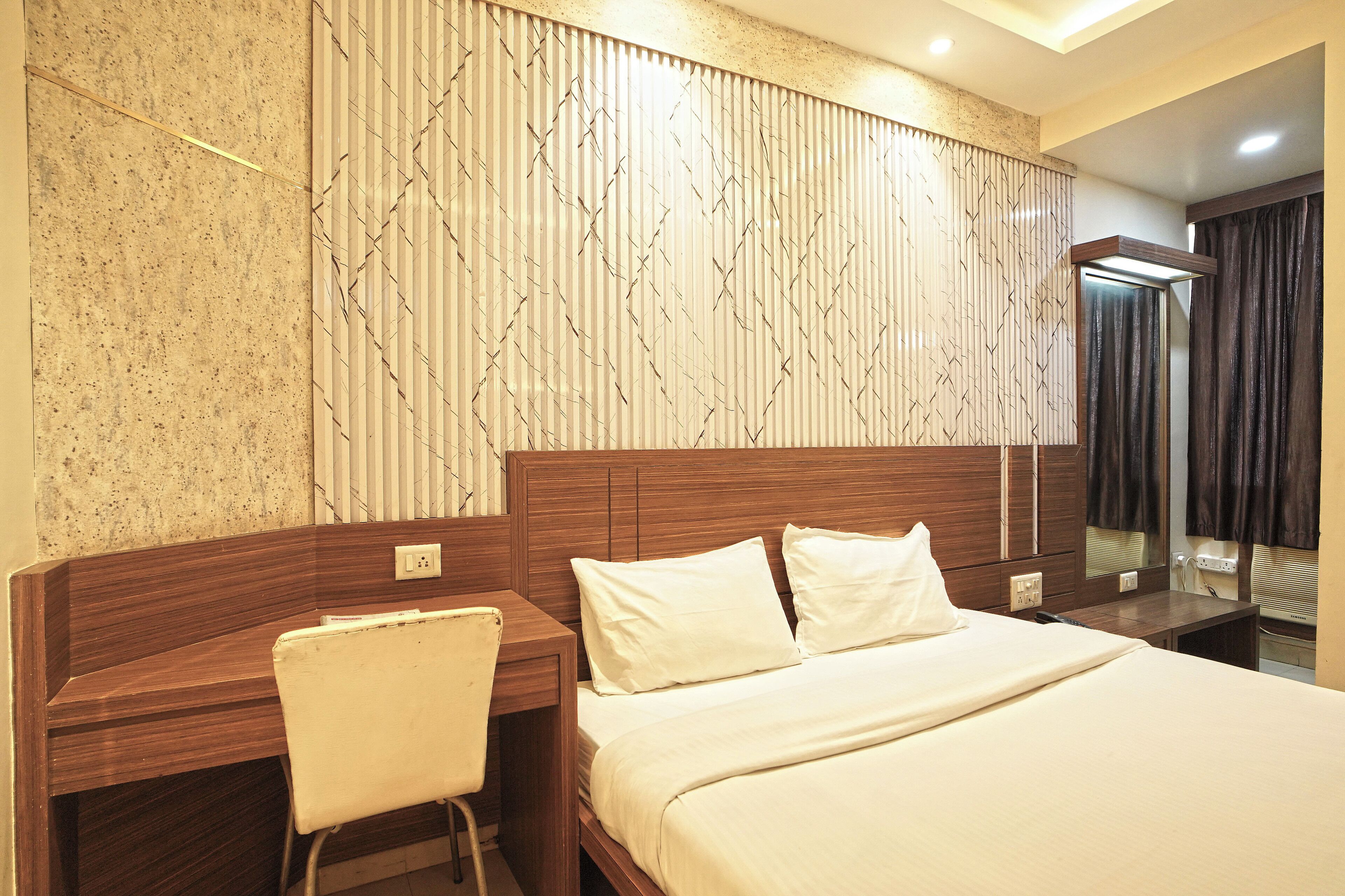 A hotel room with a wooden headboard, a bed with white linens, a desk with a chair, and a large mirror.