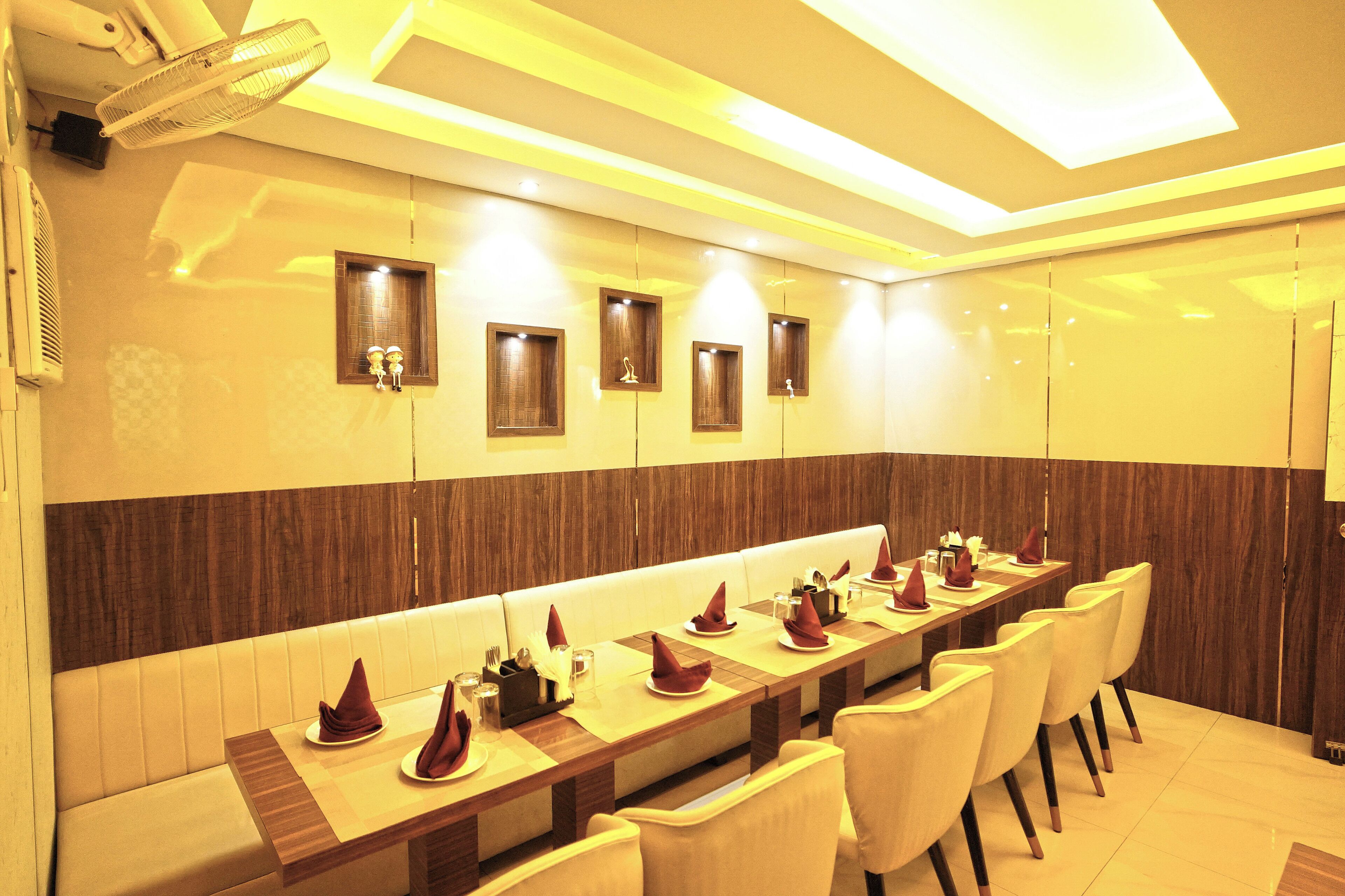 A long dining table with multiple chairs, a high ceiling with recessed lighting, and wall-mounted light fixtures.