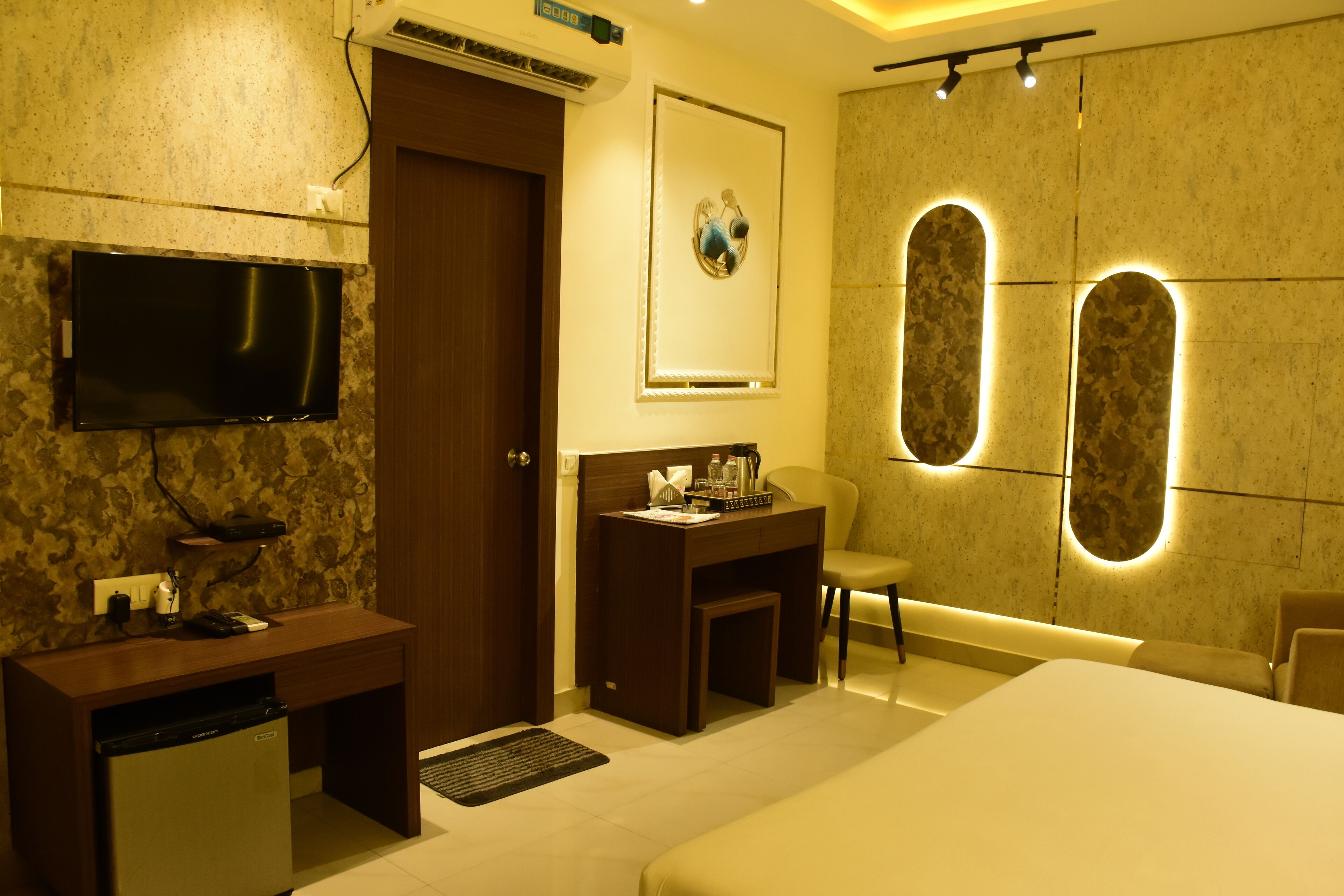 Een hotelkamer met een bed, bureau, stoel, televisie en een spiegel aan de muur.