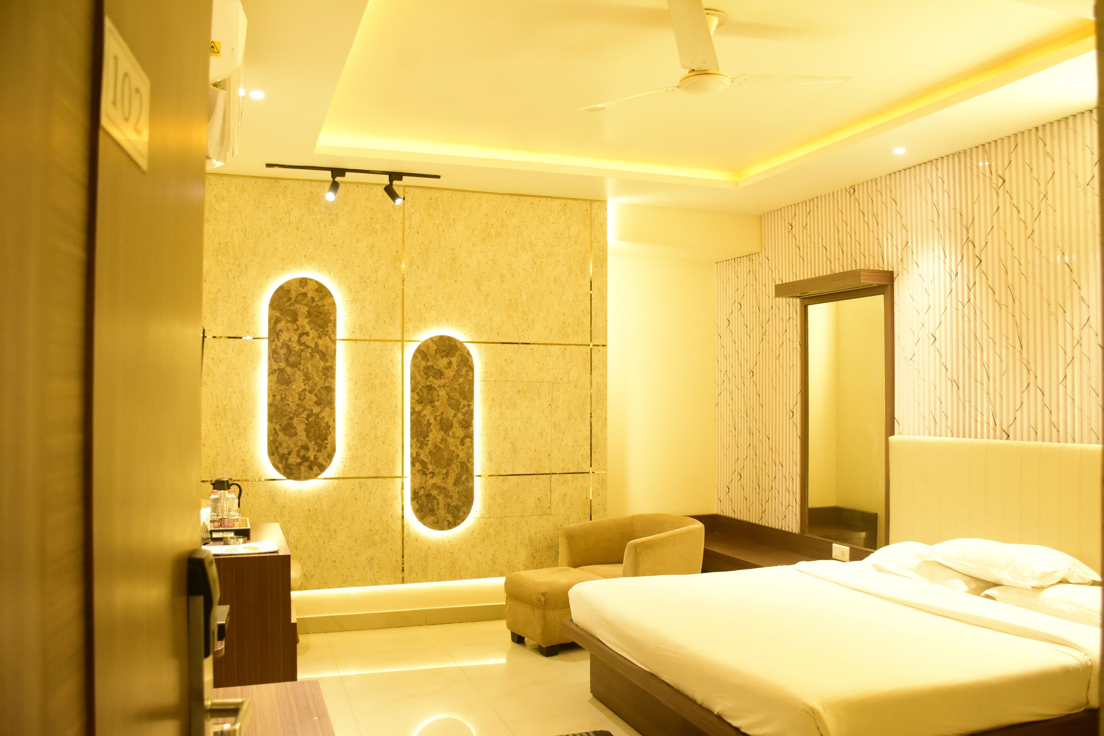 A modern hotel room with a large bed, a sitting area, and a bathroom with a vanity and mirror.