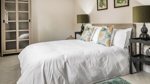 Un lit bien fait, avec du linge de lit blanc, un tapis vert et moelleux, et deux tables de chevet avec des lampes.