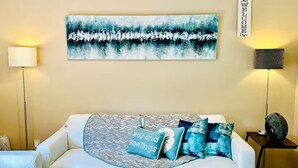 Ein modernes Wohnzimmer mit einem weißen Sofa, einem blau-weißen abstrakten Gemälde und einem 'WELCOME'-Schild an der Wand.