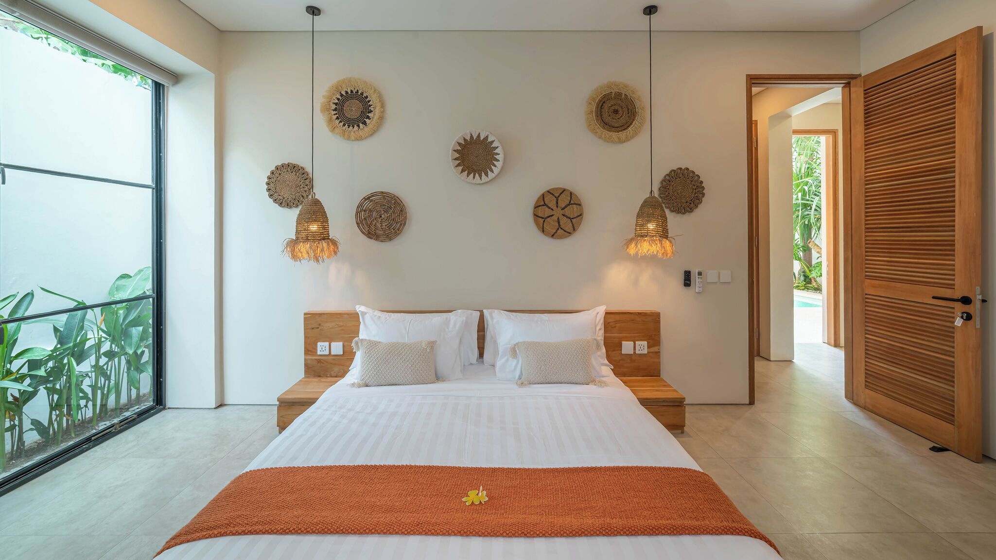 A spacious bedroom with a large bed, multiple wall-mounted lamps, and a view of greenery through a large window.