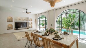 A modern dining area with a large table, wicker chairs, and a TV mounted on the wall. - Villa Unna by Elite Havens (Kerobokan)