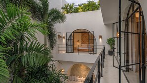 A modern hotel room with a stone accent wall, a balcony with a view of lush greenery, and a staircase leading to an upper level. - Villa Unna by Elite Havens (Kerobokan)
