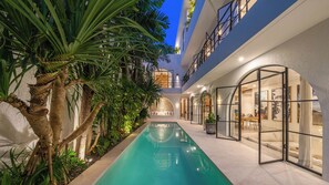 A modern indoor pool area with a clear pool, surrounded by tropical plants and a seating area with a stone wall backdrop. - Villa Unna by Elite Havens (Kerobokan)
