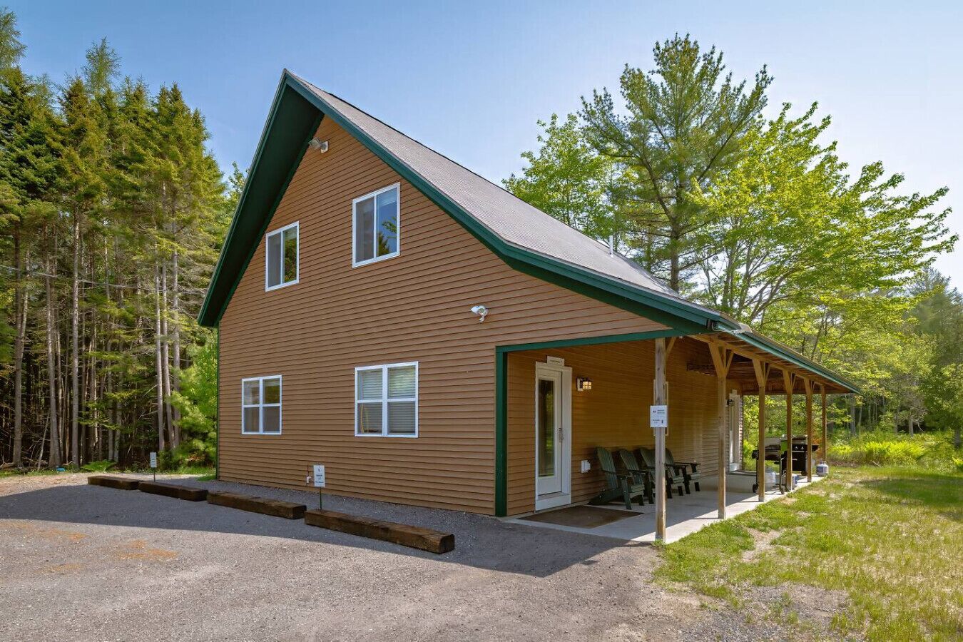 Un chalet à deux étages doté d’un porche couvert et d’une allée en gravier.