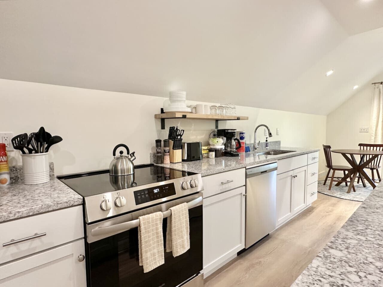 Une cuisine moderne équipée d’une cuisinière à gaz, d’un four, d’un lave-vaisselle et d’une étagère en bois au-dessus du plan de travail.