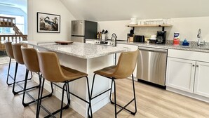 Une cuisine moderne dotée d’un îlot central, de tabourets de bar, d’appareils électroménagers en acier inoxydable et d’une grande fenêtre.