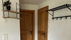 Un couloir avec une chaise en bois, une petite table, une plante posée sur une étagère et un porte-manteau.