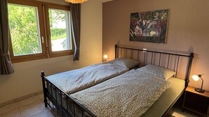 Une chambre avec deux lits, une fenêtre avec des rideaux, un tableau au mur et une lampe de chevet.