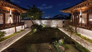 A traditional courtyard with wooden structures, a central garden, and a view of the city skyline in the background. - Nostalgia Hanok Hotel (Seoul)