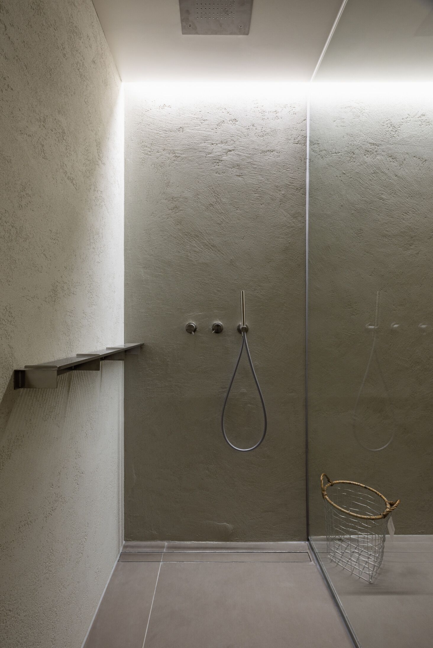 A modern shower with a glass door, a metal showerhead, and a small metal basket on the floor.