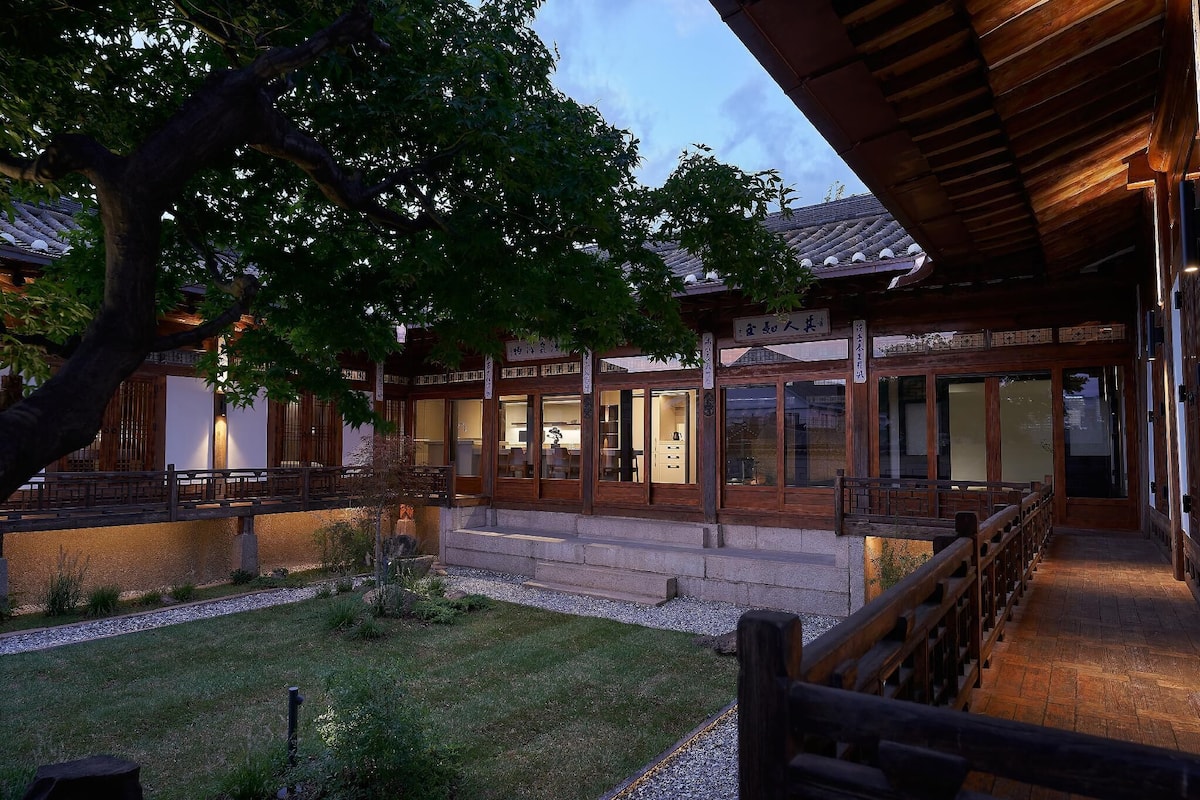 Un edificio japonés tradicional con arquitectura de madera, un sendero de piedra y un árbol en primer plano.