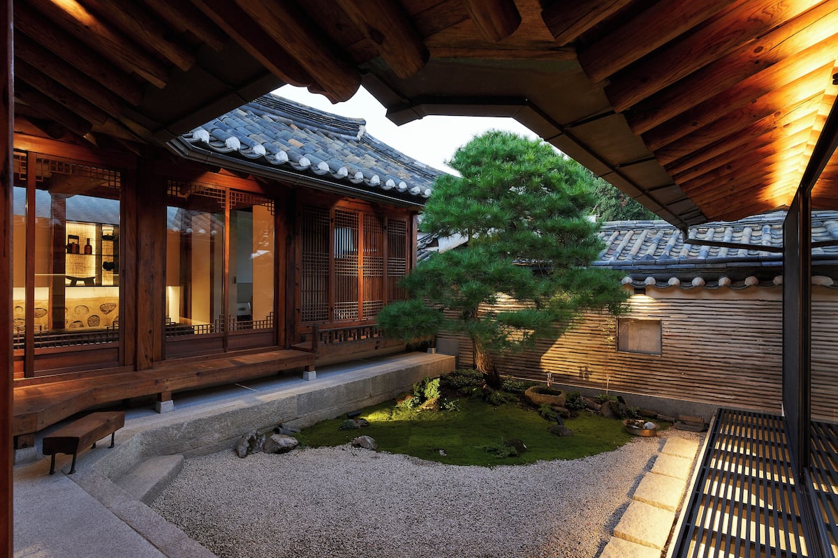 Un edificio japonés tradicional con arquitectura de madera, un sendero de piedra y un jardín bien cuidado con un pino.