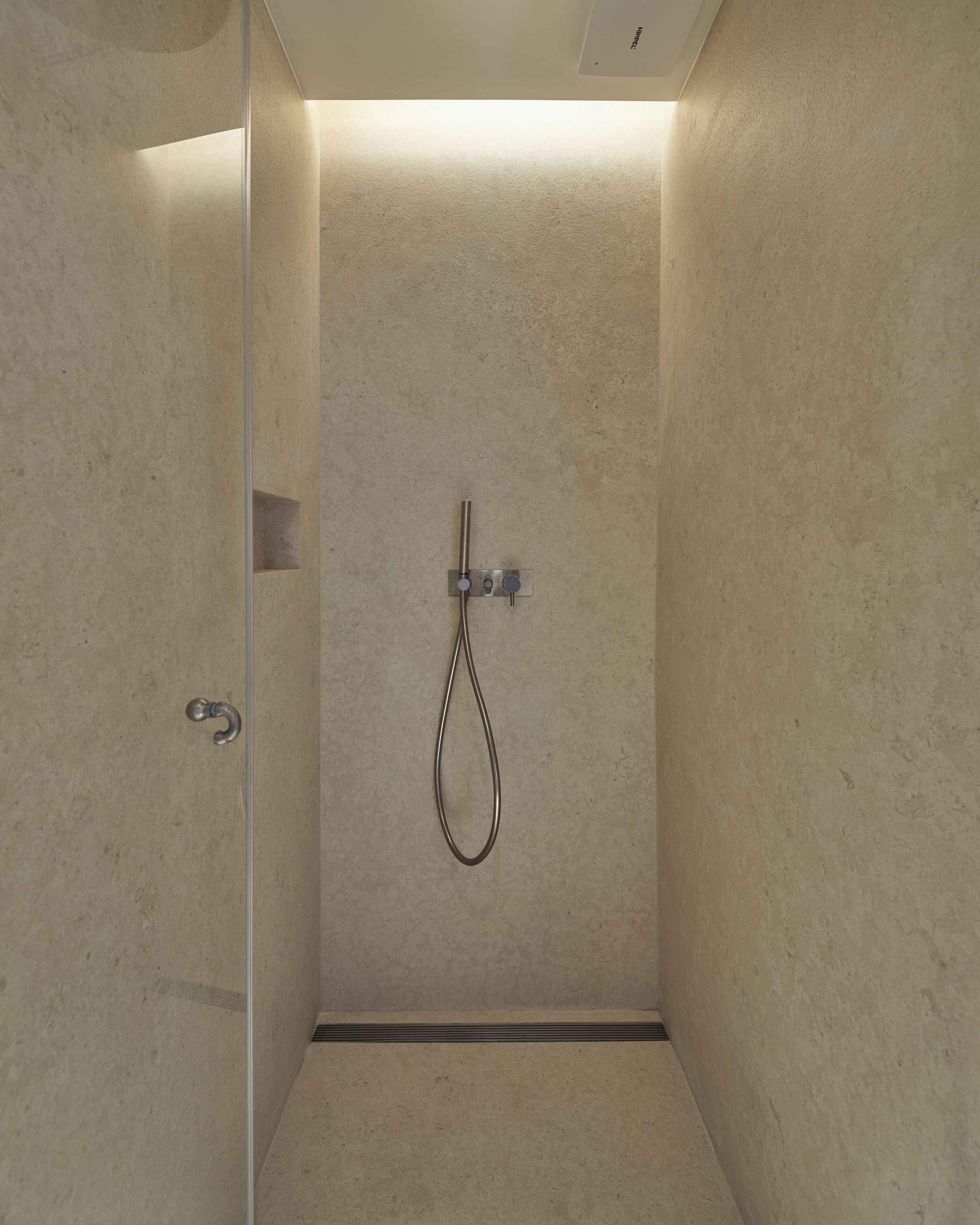 Una ducha moderna con cabezal de ducha de mano, panel de control en la pared y suelo de azulejos.