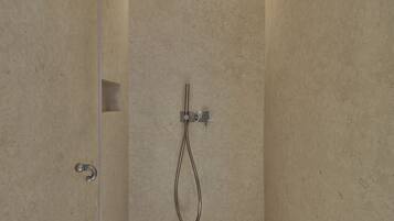 Una ducha moderna con cabezal de ducha de mano, panel de control en la pared y suelo de azulejos.