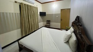 Een hotelkamer met een bed, een plafondventilator, een airconditioner, een televisie, een stoel en een deur.