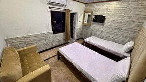 Een hotelkamer met twee bedden, een bank, een airconditioner, een plafondventilator en een klein raam met gordijnen.