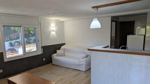 A modern living room with a white sofa, a wooden coffee table, and a kitchen area with a white refrigerator.